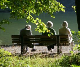 Three older people sitting on a bench in front of a lake